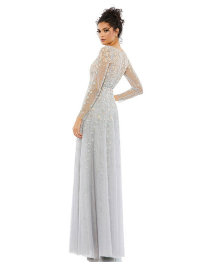 This gorgeous surplice gown is crafted with a sheer mesh overlay adorned with 3D floral embellishments across the bodice, arms, and skirt. With a v-neckline, sheer long sleeves, and a flowing skirt, this dress is an elegant choice for your next event. Mac