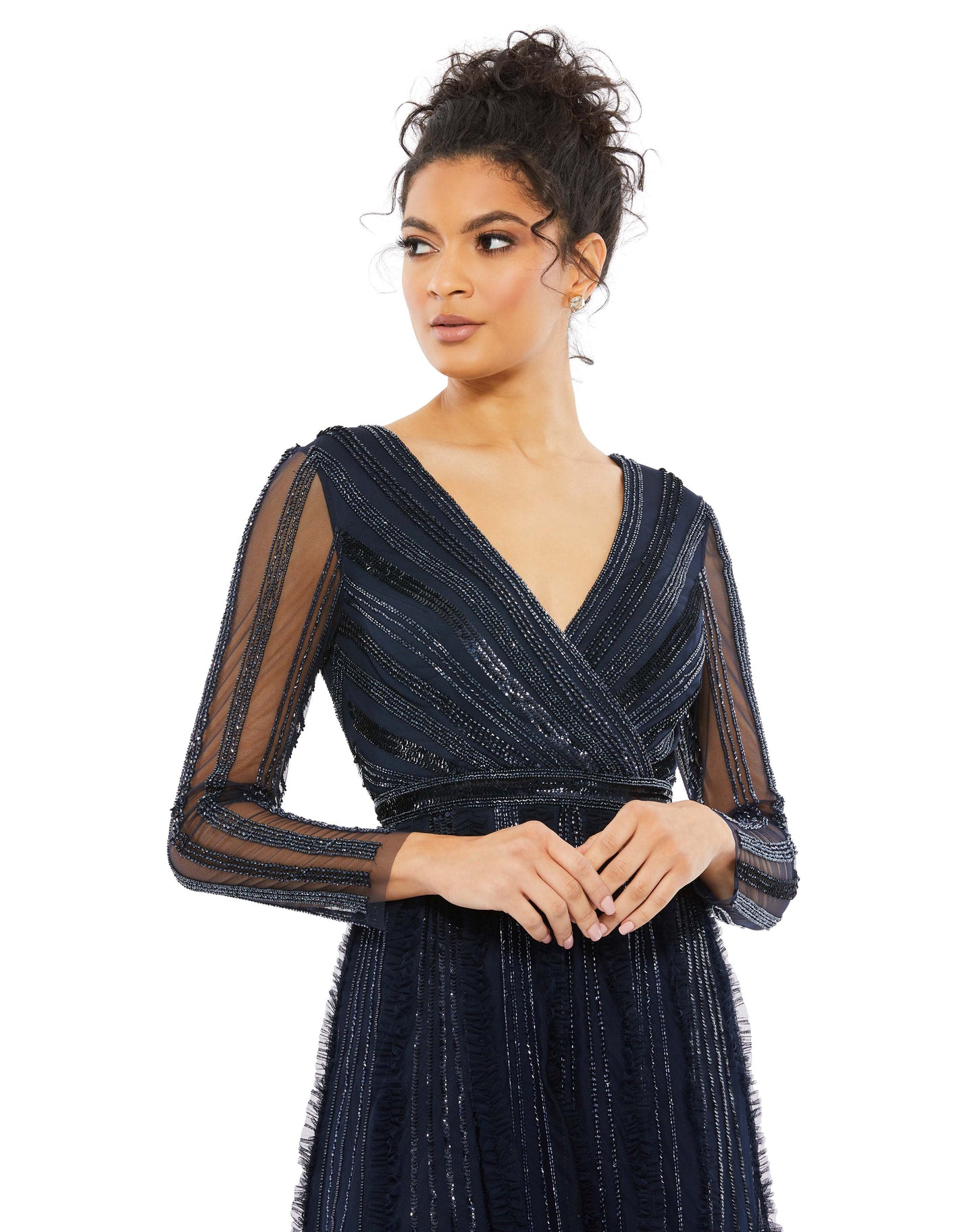 Elegant evening gown with a faux-wrap v-neckline, long illusion sleeves, and a floor-length skirt. The bodice and sleeves feature rows of sequins and beads throughout the mesh, and the skirt is embellished with elongating rows of beads, sequins, and subtl