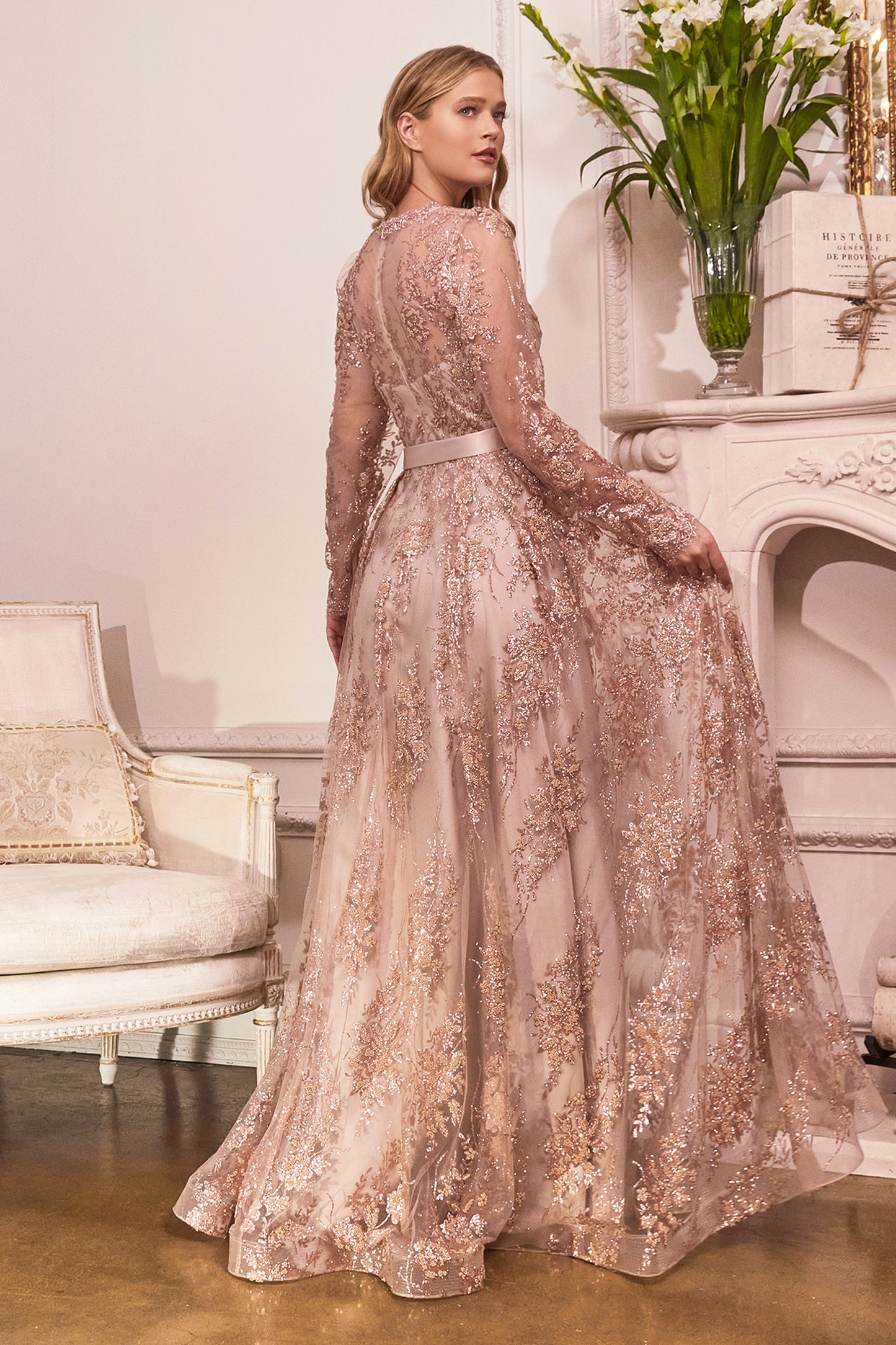 Make a grand entrance in this modest long sleeve gown. A shimmering glitter floral print adorns the fabric flowing from a lace scalloped v-neckline into an a-line layered skirt. The center back is closed with a zipper allowing for more coverage and wrist